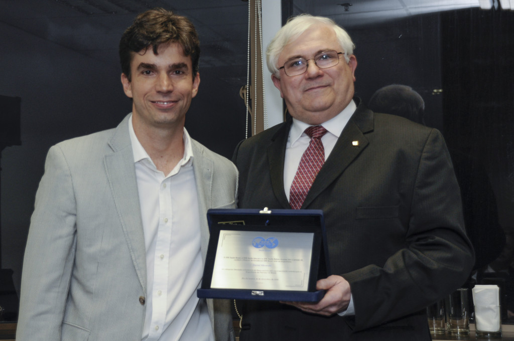 Luiz Otávio Schmall entrega placa de premiação a Daniel Miranda.